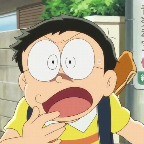 Nobita áp tay lên miệng với mắt mở to, chiếc áo vàng sáng màu làm biểu cảm sửng sốt nổi bật như vừa nghe tin sét đánh