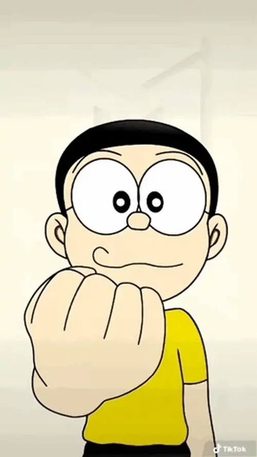 Nobita mặc áo vàng giơ nắm đấm sát mặt, đôi mắt tròn sau kính tạo vẻ quyết liệt nhưng vẫn buồn cười theo kiểu cậu bé hậu đậu
