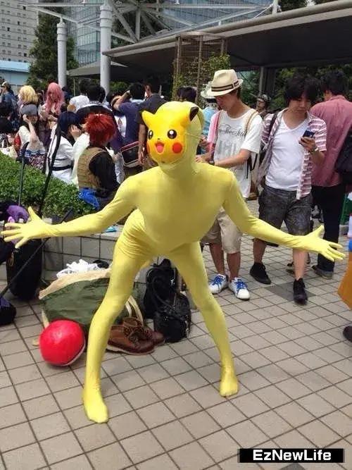 Mascot Pikachu dáng người cao gầy đứng giữa khu phố đông, hai tay dang rộng với quả bóng đỏ dưới chân