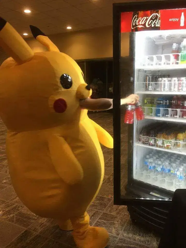 Tượng Pikachu vàng ngồi cạnh tủ nước trong góc cửa hàng, ánh đèn ấm làm khuôn mặt tròn thêm ngơ ngác
