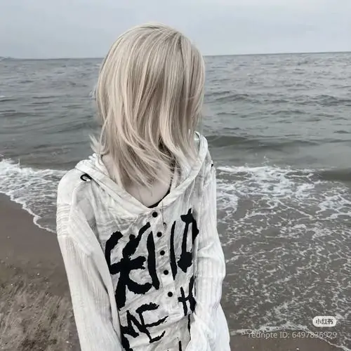 Cô gái tóc bạch kim đứng quay lưng bên bờ biển xám, áo hoodie trắng có chữ đen hợp nữ thích ảnh diện mạo kỹ thuật số buồn