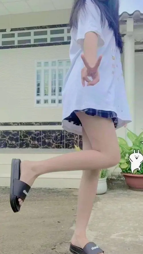 Giữa khung cảnh ngoài trời xanh sáng, cô gái áo trắng phối váy ngắn tạo dáng nhấc chân, tóc dài buông tự nhiên sau lưng