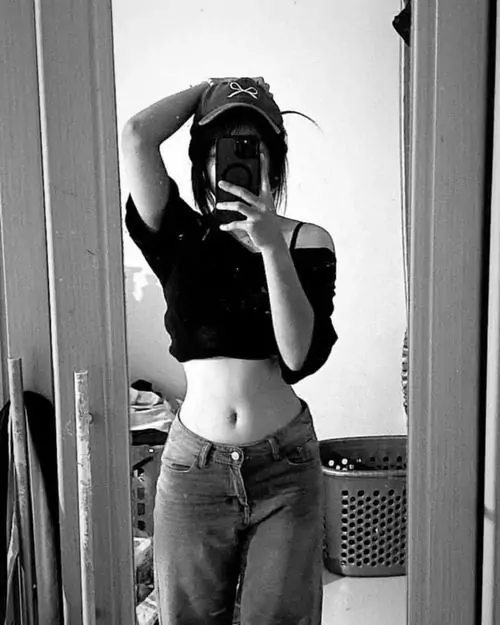 Khung ảnh đen trắng cho thấy cô nàng tạo dáng trước gương, áo croptop tối màu và quần jean nhấn vào eo gọn