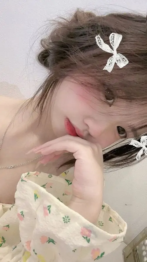 Cô gái ngồi bên giỏ hoa ngoài trời, váy họa tiết nhẹ, tóc dài buông vai và ánh mắt nhìn nghiêng tạo cảm giác thân thiện