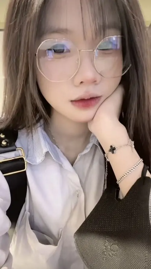 Tai nghe trắng nổi bật trên mái tóc dài, hình nữ sinh trong trẻo mặc áo đen, đưa tay chỉnh tóc và nhìn thẳng ống kính
