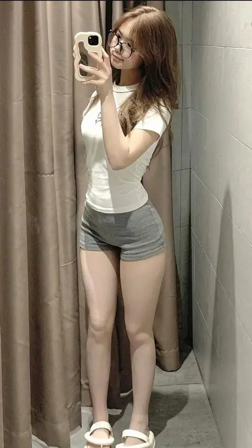 Góc chụp trước gương ghi lại hình ảnh mỹ nhân quyến rũ mặc áo trắng cùng quần short xám, tóc nâu xoăn nhẹ rất trẻ trung