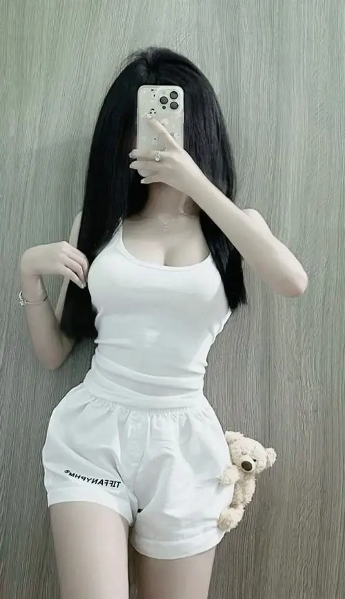 Trong khung hình selfie trước gương, cô gái mặc set trắng ôm dáng, tóc dài che một phần mặt và đứng nghiêng rất duyên