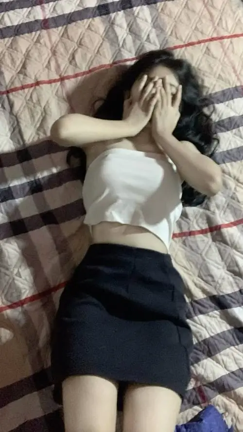 Không gian trong phòng phủ tông caro ấm, cô gái mặc áo trắng cùng chân váy đen, tay vuốt tóc tạo dáng mềm mại