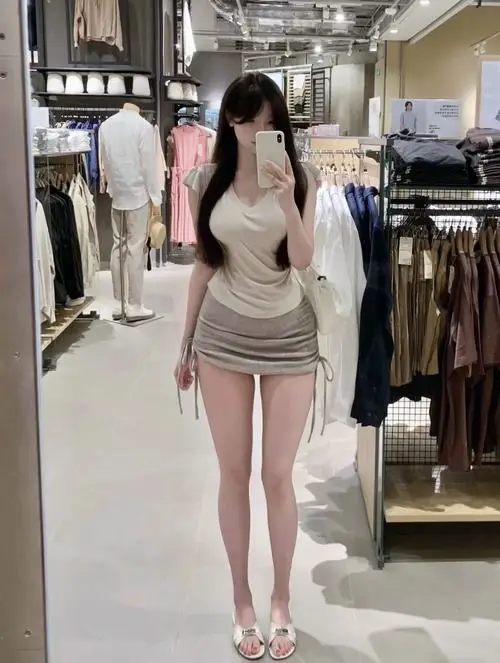 Trong cửa hàng thời trang sáng màu, cô gái diện áo trắng cùng chân váy ngắn, đứng quay lưng nhẹ và khoe mái tóc dài