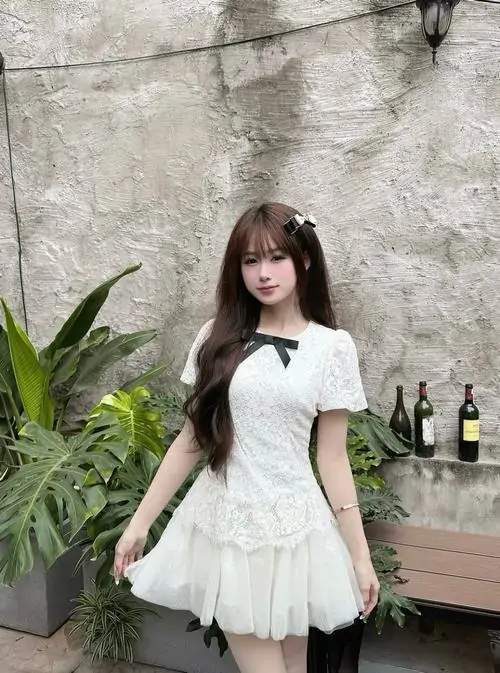 Nền tường xám và chậu cây xanh làm cô gái váy trắng thêm nổi, tóc dài buông vai và dáng đứng rất hiền