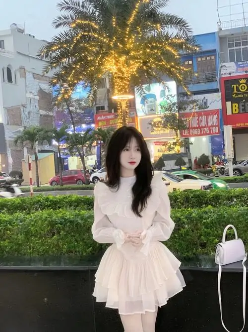 Giữa góc phố sáng đèn, cô nàng mặc váy trắng xếp tầng đứng yên, mái tóc ngắn và túi nhỏ tạo vẻ trẻ trung