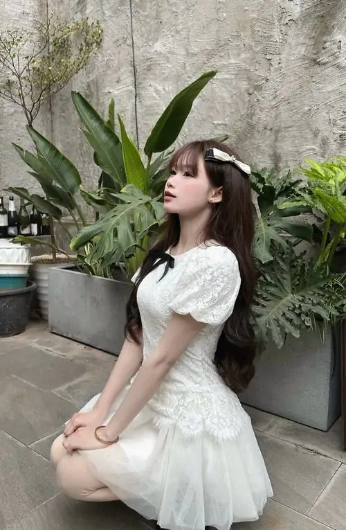 Bậc thềm đá phủ cây xanh làm hình ảnh hot girl váy trắng ngắn thêm dịu, cô nàng ngồi nghiêng với tóc dài uốn nhẹ