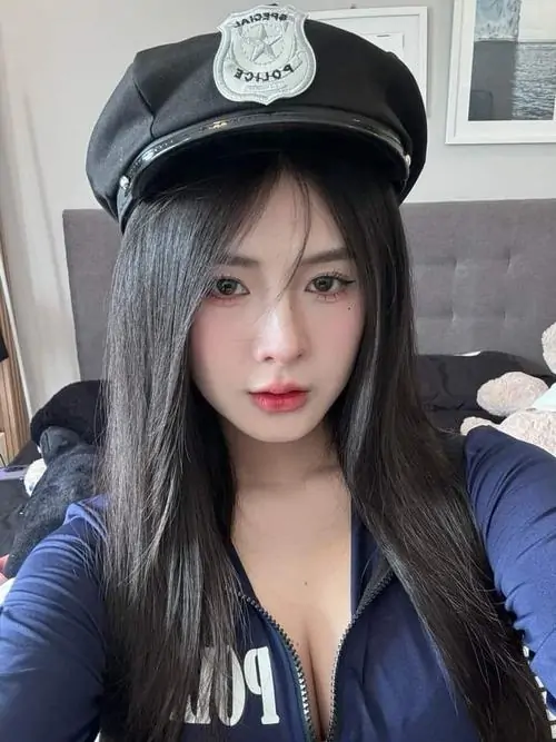 Cô gái đội mũ cảnh sát tạo dáng nhìn thẳng, tóc đen dài ôm gương mặt thanh tú, trang phục tối màu làm thần thái thêm sắc sảo