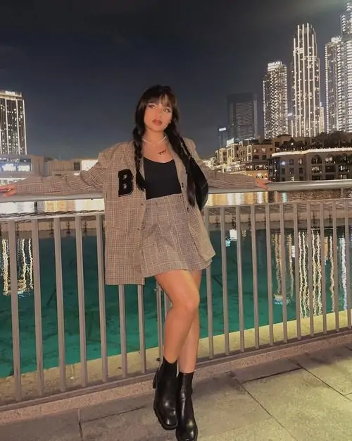 Bên lan can đêm đô thị, ảnh hot girl quốc tế cho thấy cô gái mặc áo đen váy xám tạo dáng, mái tóc dài nổi bật trên nền phố