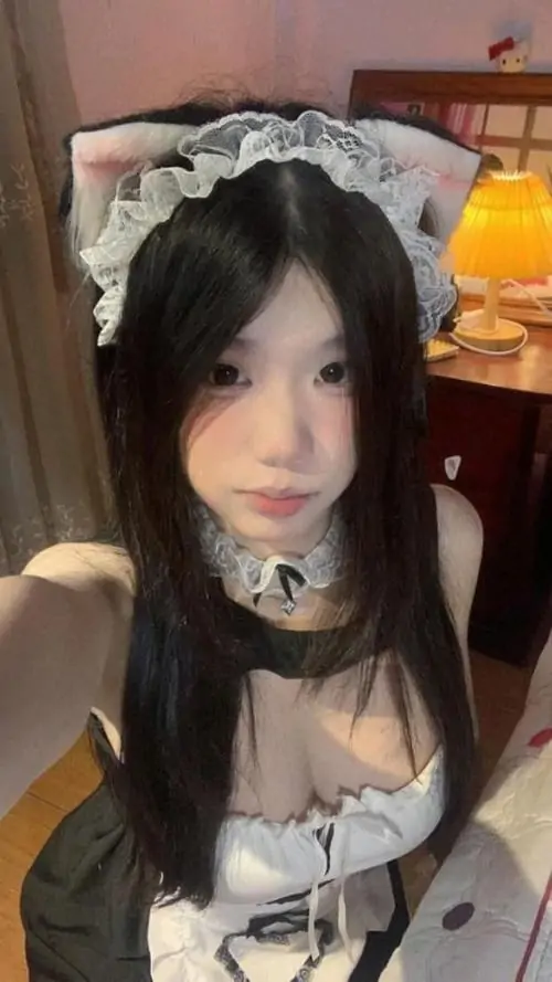 Ánh đèn ấm phía sau làm gương mặt cô gái thêm mềm, nơ cổ đen và tạp dề ren tạo điểm nhấn ngọt ngào