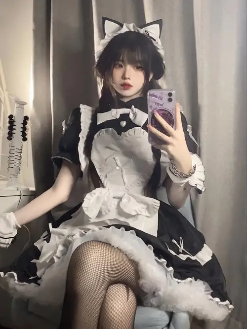 Trong ảnh selfie trước gương, cô gái ngồi vắt chân nhẹ, váy hầu gái xếp tầng và tất lưới tạo cảm giác cổ điển pha hiện đại