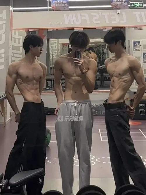 Ba dáng đứng trước gương tạo thành hình ảnh múi bụng nam rõ nét, quần đen rộng và cơ bụng đối xứng trong phòng tập