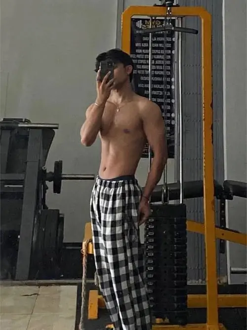 Chàng trai chụp gương trong phòng gym, lưng trần quay về ống kính, quần kẻ ô rộng và bờ vai rắn rỏi nổi bật