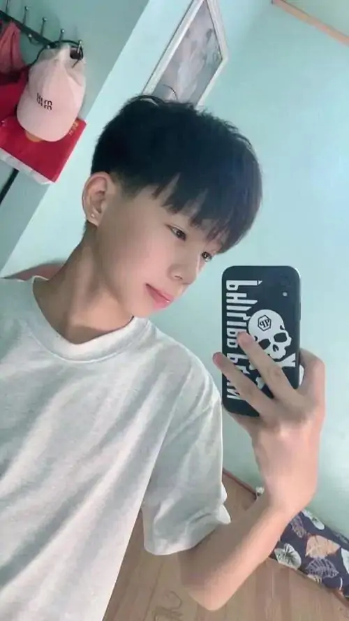 Gương phòng phản chiếu bạn nam áo trắng cầm điện thoại selfie, tóc cắt gọn, khuôn mặt nghiêng nhẹ và phong thái rất tự nhiên