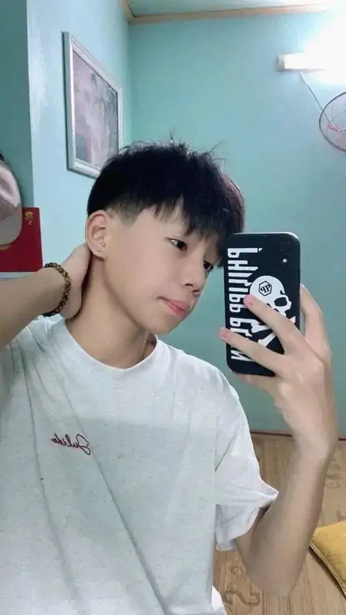 Góc selfie trước gương ghi lại bạn nam áo trắng, tóc cắt gọn hai bên, dáng nghiêng nhẹ tạo cảm giác sạch sẽ và đời thường