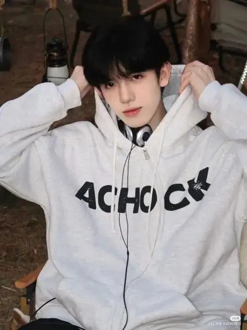 Áo hoodie trắng kéo cao hai tay tạo nét đáng yêu cho bạn nam 2011, tóc đen mềm ôm mặt và ánh nhìn thẳng khá ngoan