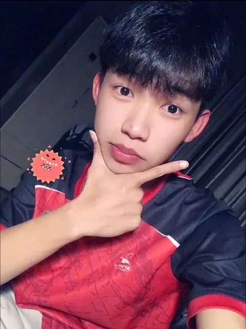 Áo đấu đỏ đen làm cậu bạn K12 nổi bật dưới ánh đèn tối, tay chống cằm và nụ cười mím khá tinh nghịch