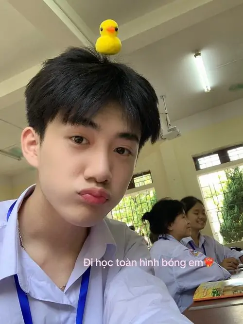 Chú vịt vàng trên đầu tạo điểm vui cho cậu bạn áo trắng, môi chu nhẹ và ánh mắt nhìn máy mang nét tinh nghịch