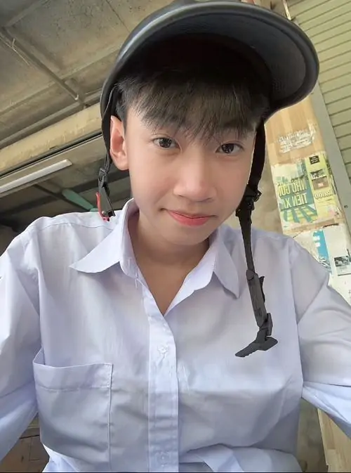 Đồng phục trắng cùng mũ lưỡi trai đen giúp bạn nam ngồi trong xe trông gọn gàng, tóc mái ngắn và nụ cười nhỏ