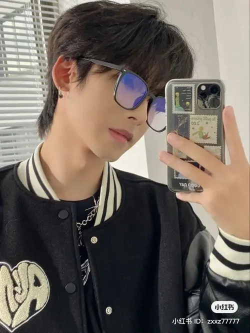 Góc selfie trước gương cho thấy bạn nam áo khoác bóng chày đen, đeo kính màu, tóc vuốt lệch và dáng cầm máy khá tự tin