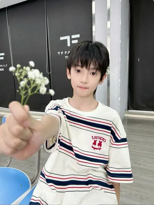Bó hoa nhỏ đưa sát ống kính làm khung ảnh mềm hơn, cậu bạn áo sọc trắng đỏ cười nhẹ với mái tóc đen gọn