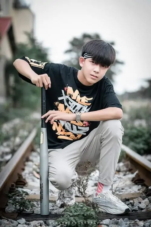 Trên đường ray cũ, bạn nam áo thun họa tiết ngồi tạo dáng thoải mái, quần xám và sneaker trắng làm ảnh có chất streetwear