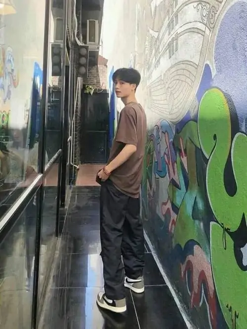 Bức hình trong không gian graffiti có chàng trai tuổi teen mặc áo nâu đứng nghiêng, tóc đen gọn và dáng nhìn xa khá tự nhiên