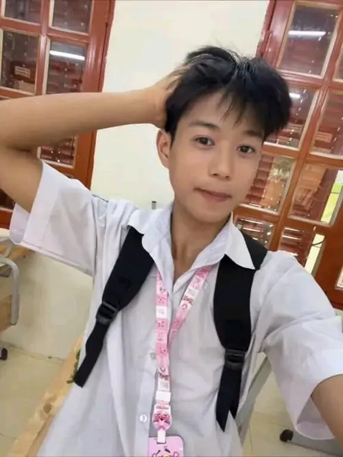 Chàng trai mặc áo sơ mi trắng đang vuốt tóc với nụ cười rạng rỡ.