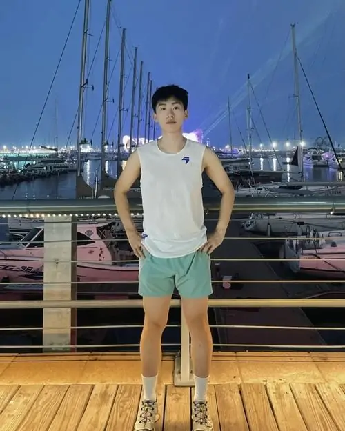 Chàng trai mặc áo ba lỗ trắng đứng tự tin trên bến cảng lúc chiều tà với ánh sáng dịu nhẹ bao quanh.
