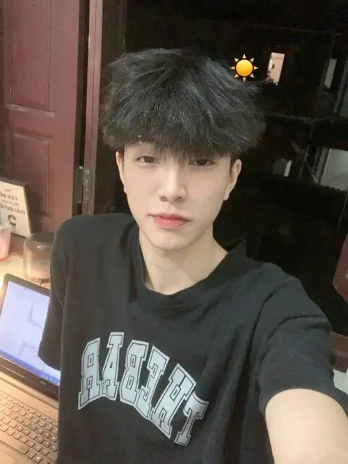 Thiếu niên mặc áo đen in chữ đang selfie trong phòng với ánh sáng dịu.