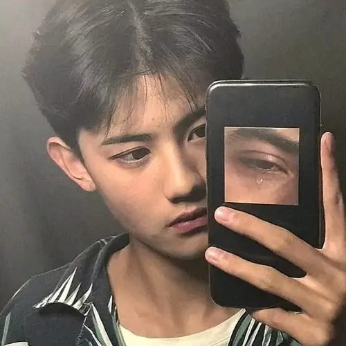Thiếu niên mặc áo hoodie đang cầm điện thoại selfie trong gương với ánh sáng tự nhiên.