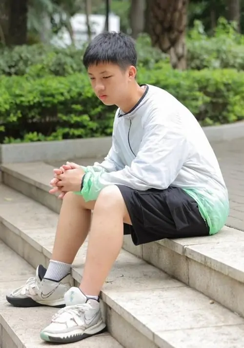 Cậu bé mặc áo hoodie trắng ngồi nghỉ trên cầu thang ban đêm với ánh đèn neon.