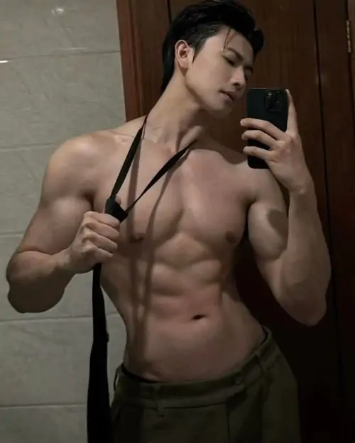 Chàng trai đẹp 6 múi Việt selfie trước gương, mặc quần đen và dây áo chéo, cơ bụng rõ rãnh cùng nét mặt tập trung