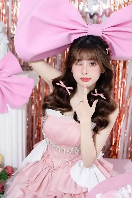Phông hồng gắn nơ lớn phía sau làm nổi bật cô gái tóc nâu, áo ôm màu pastel và dáng đứng tự tin