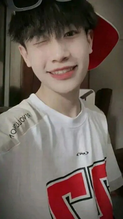 Nụ cười tươi làm cậu bạn áo trắng viền đỏ nổi bật, tóc đen mềm và nền trong nhà tạo cảm giác ấm áp