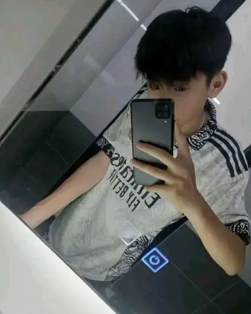 Góc selfie trong thang máy ghi lại cậu bạn áo sọc thể thao, tay cầm điện thoại che mặt và tóc đen phủ trán