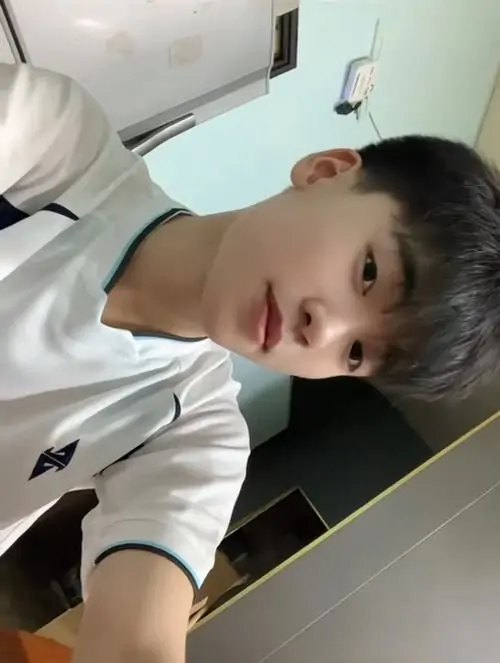 Góc chụp nghiêng từ dưới lên bắt được cậu bạn áo trắng trong phòng, tóc cắt gọn và ánh mắt nhìn máy hơi tò mò