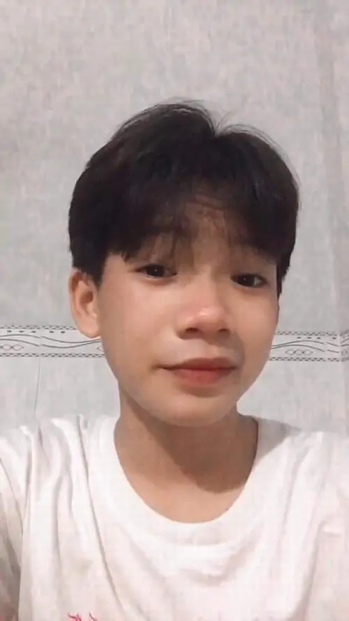 Nền tường gạch sáng phía sau làm gương mặt cậu bạn 2013 áo trắng nổi hơn, tóc ngắn gọn và môi cười mím