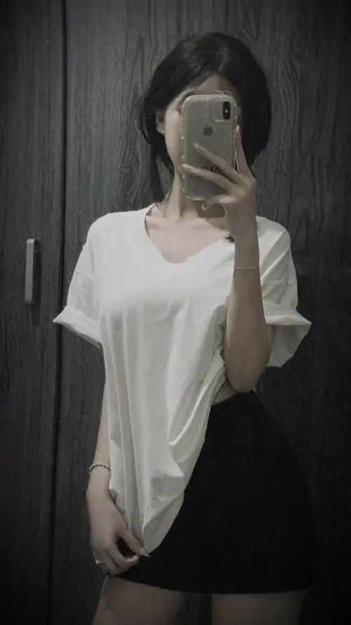 Ánh gương tối làm cô gái áo thun trắng dáng rộng trông mềm hơn, mái tóc dài xõa xuống vai trong tư thế đứng yên
