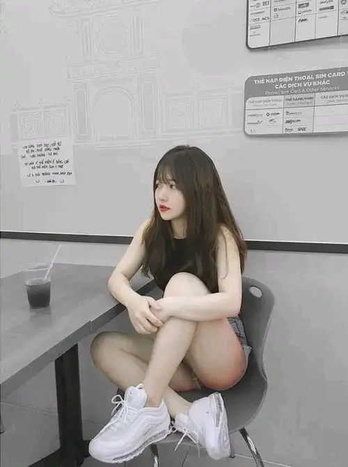 Cô gái áo trắng ngồi trên máy tập trong ảnh gái xinh chụp dáng, đôi vớ cao và giày thể thao tạo nét năng động