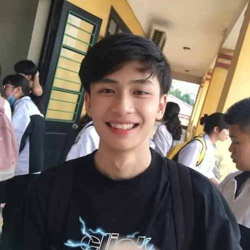 Chàng trai trẻ mặc áo thể thao đang đứng ngoài trời với nụ cười tươi tỉnh và mái tóc gọn gàng.