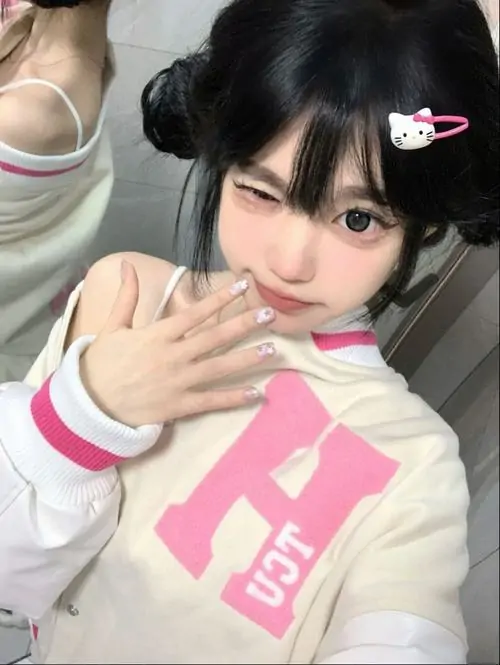 Váy ngủ lụa hồng ôm nhẹ cơ thể, cô gái ngồi bên rèm trắng với bờ môi mọng và ánh mắt dịu
