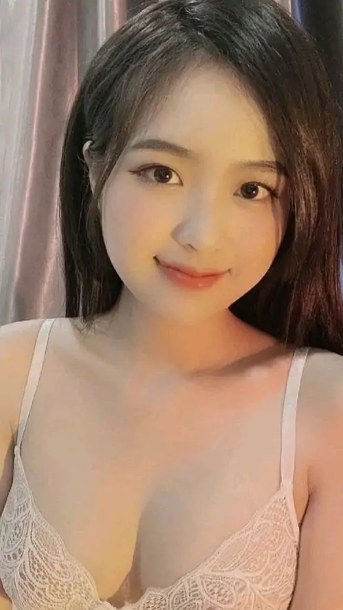 Cô gái mặc áo hai dây trắng ngồi trong nắng nhẹ, tóc đen dài buông thẳng và nụ cười nhỏ tạo cảm giác gần gũi