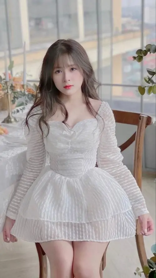 Cô gái mặc đầm dạ hội đỏ đứng dưới ánh đèn, mái tóc xoăn dài và nụ cười tự tin làm tổng thể rất sang