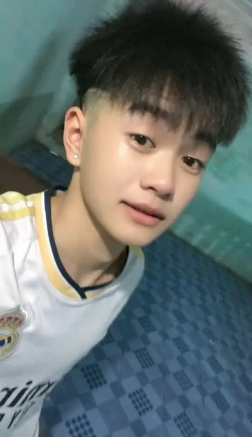 Sân bóng phía sau làm cậu bạn 2013 mặc áo thể thao đỏ trắng trông khỏe khoắn, tóc mái ướt nhẹ và dáng đứng thoải mái